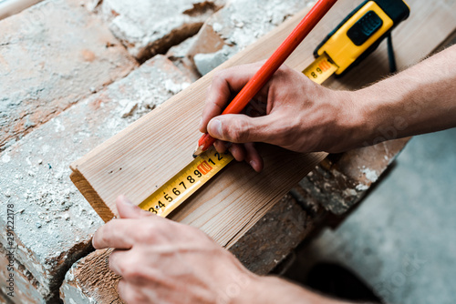 cropped view of repairman holding pencil while measuring wooden plank