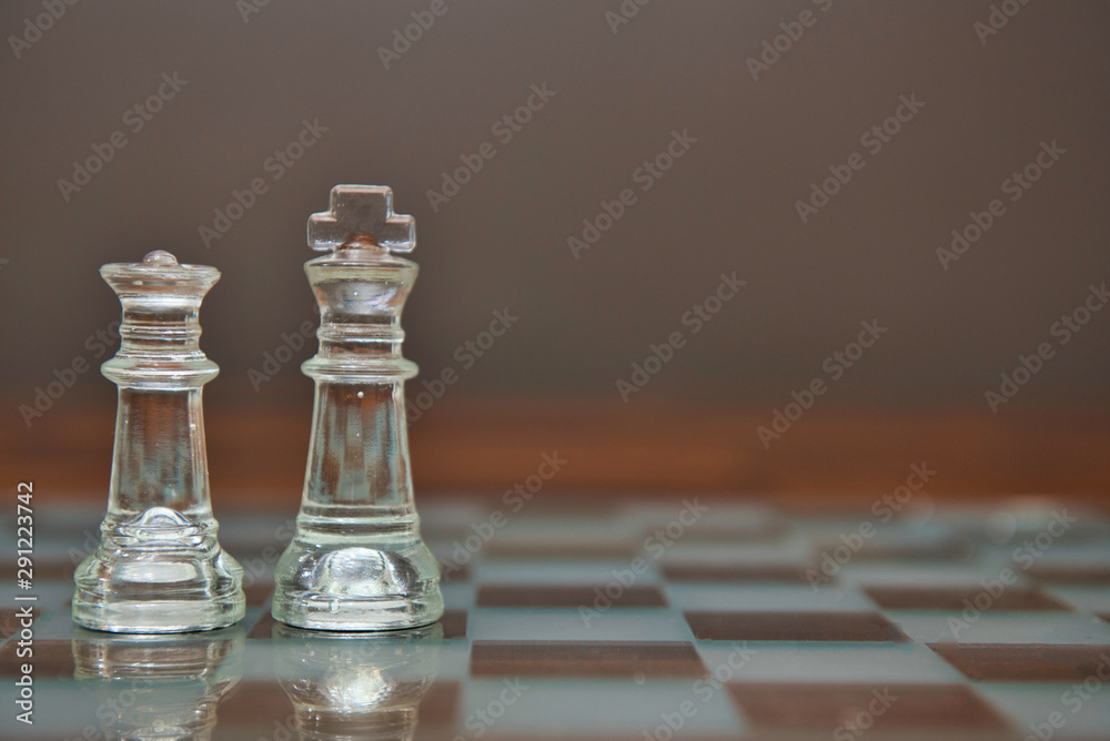 King and Queen pieces on a glass chess board King and Queen pieces on a glass chess board
