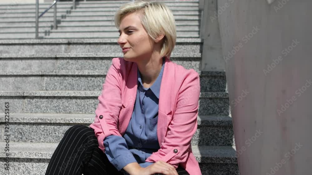 Gorgeous woman sitting on the stairs and relying on her elbow while daydreaming. Blonde woman smiling and playing with her short hair. Gorgeous woman sitting on the stairs and relying on her elbow while daydreaming. Blonde woman smiling and playing with her short hair.