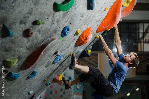 strong healthy sport caucasian man with beard and eyeglasses climbing on wall indoors during bouldering exercise