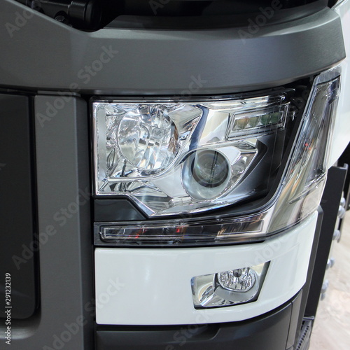 Closeup front view on left headlight of new black-white modern truck - transportation logistics, goods delivery on road transport