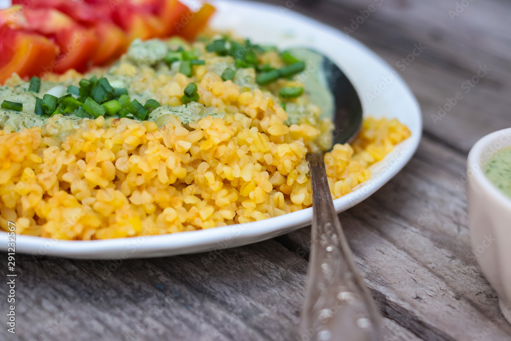 Bulgur with sauce, greens, tomatoes on plate. Vegan lunch.