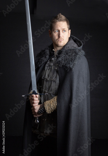 Medieval  or post apocalyptic man in leather jerkin and cloak wielding a sword and dagger photo