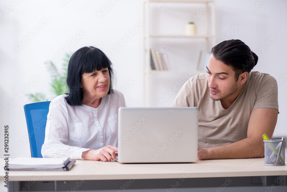 Young male employee explaining to old female colleague how to us Young male employee explaining to old female colleague how to us