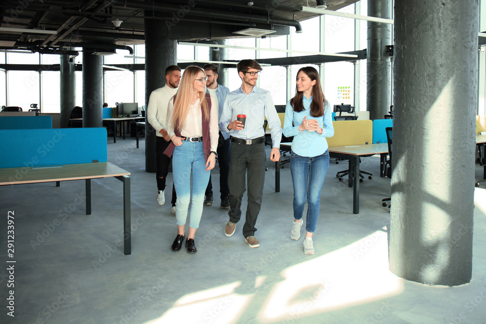 Full length of young people in smart casual wear discussing business and smiling while walking through the office.