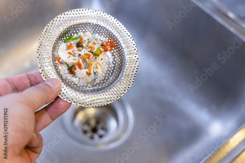 Hand holding kitchen sink waste filter with trapped food waste