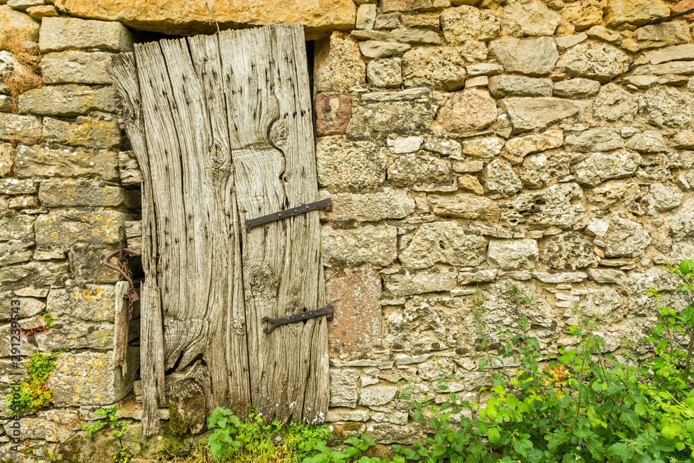 An old wooden door ill-fitting on the stone wall of a farm in Lozère, France An old wooden door ill-fitting on the stone wall of a farm in Lozère, France