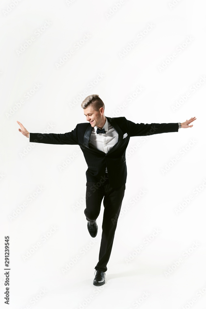 Portrait of young smiling handsome man in tuxedo stylish black suit, studio shot isolated on white background. Showman or toastmaster in jacket with bowtie