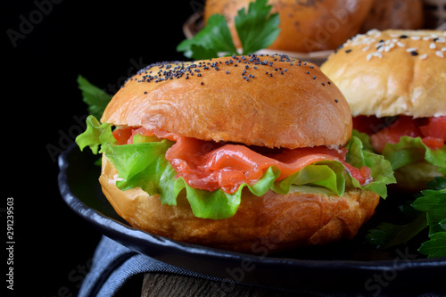 Bagel sandwich with smoked salmon and lettuce salad on black plate