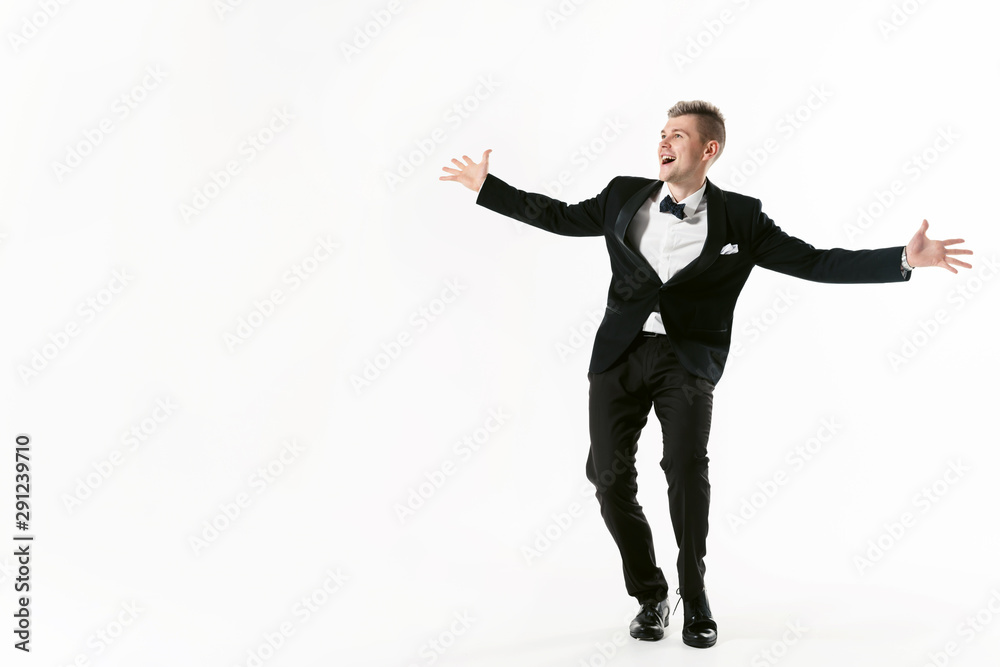 Portrait of young smiling handsome show man in tuxedo stylish black suit, studio shot dancing at white background. Businessman in jacket with bowtie Portrait of young smiling handsome show man in tuxedo stylish black suit, studio shot dancing at white background. Businessman in jacket with bowtie