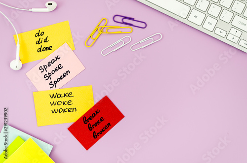 Foto Top view desk with earphones, keyboard and sticky notes with handwritten irregular verbs
