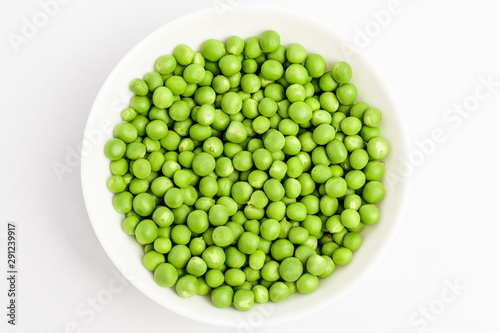 Freeh organic green peas in a white round bowl on a table in soft focus, isolated on white, top view photo