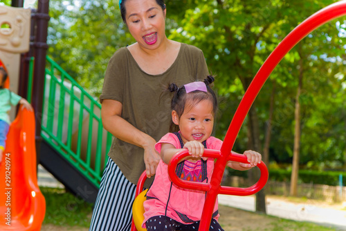 Mom and daughter  playing on play ground play slider seesaw,  Funny Asian family in a park photo