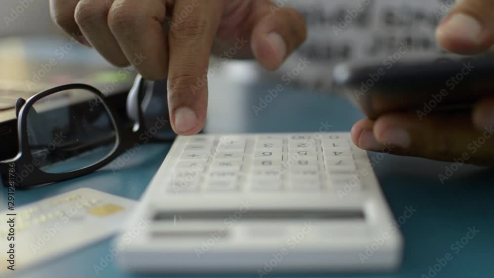Hands of a man calculating expenses from credit card while using mobile phone data.