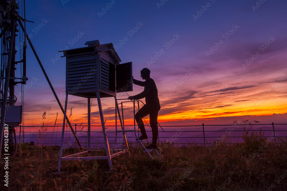 man at weather station in sunset mountain landscape. - obrazy, fototapety, plakaty 