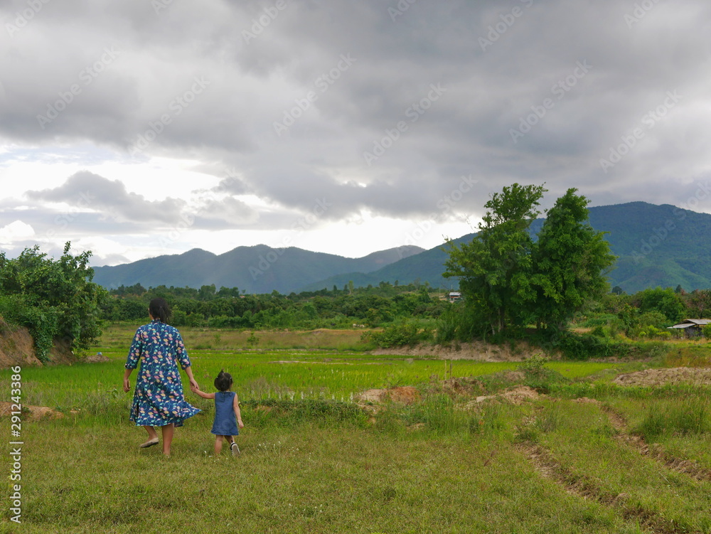 Mother holding her little baby girl's hand walking in a field in a countryside, watching rainy clouds forming in the sky- watching and learning about nature with your child