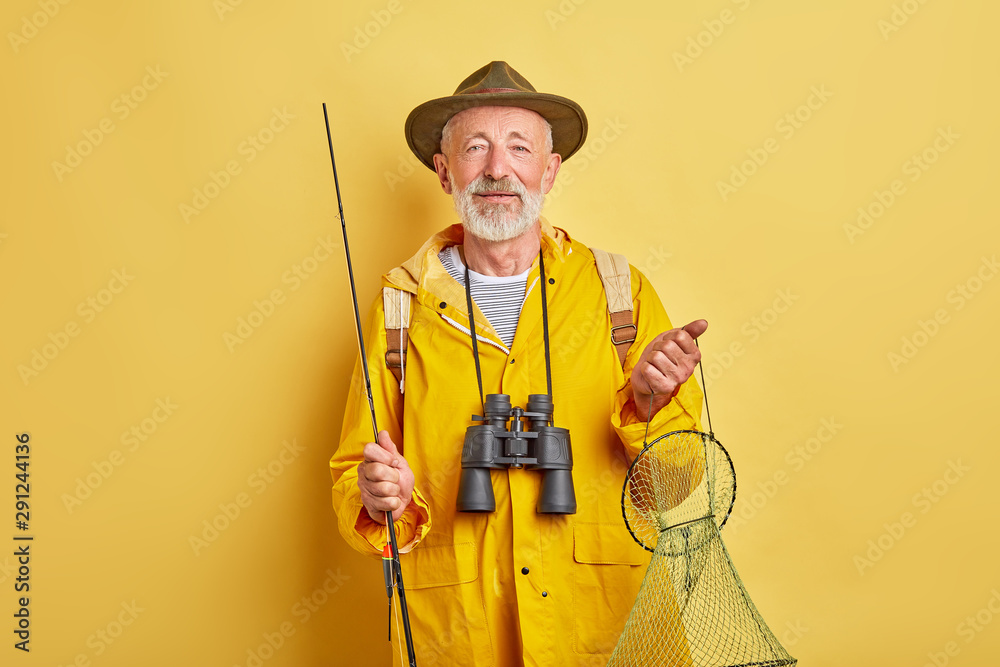 senior man has prepared to go fishing. close up photo. isolated yellow background, man holding fishing equipment senior man has prepared to go fishing. close up photo. isolated yellow background, man holding fishing equipment