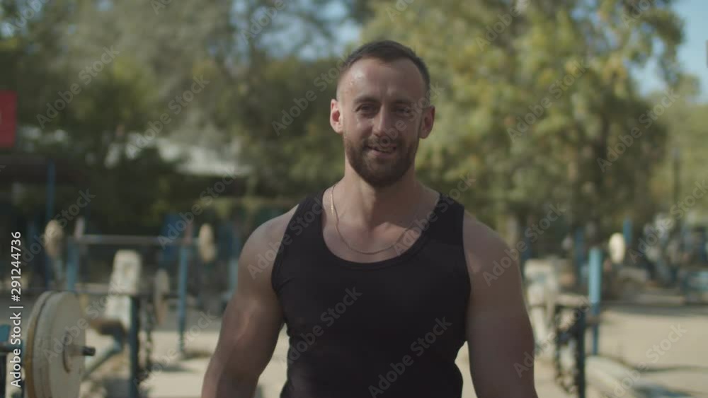 Portrait of handsome smiling athletic fit man with perfect muscular body walking along rows of exercise machines before strength weight training in outdoor gym, expressing confidence and positivity. Portrait of handsome smiling athletic fit man with perfect muscular body walking along rows of exercise machines before strength weight training in outdoor gym, expressing confidence and positivity.