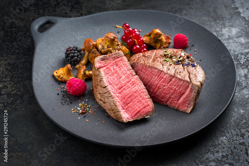 Gebratenes dry aged Rinderfilet Medaillon Steak natur mit Pfifferlingen und Waldbeeren angeboten als closeup auf einem Modern Design Teller und rustikalen Hintergrund  photo