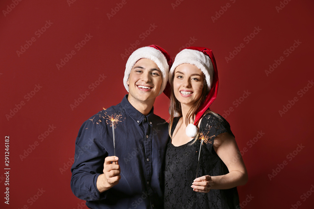 Happy young couple with Christmas sparklers on color background Happy young couple with Christmas sparklers on color background
