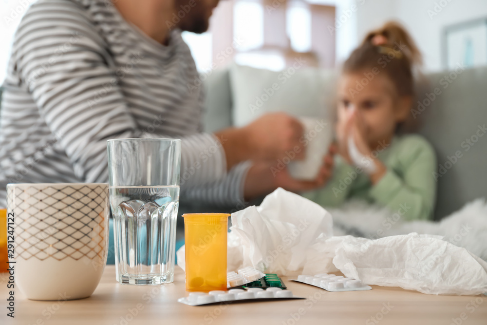 Medicines on table and blurred father taking care of his sick daughter on background Medicines on table and blurred father taking care of his sick daughter on background