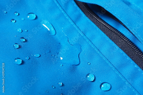 Closeup of water drops on bright blue fabric and black zipper with waterproof design to protect fabric of the cloth from humidity and to offer easy cleaning to users Fabric texture with design concept