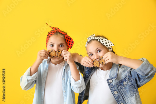 Portrait of funny twin girls with cookies on color background