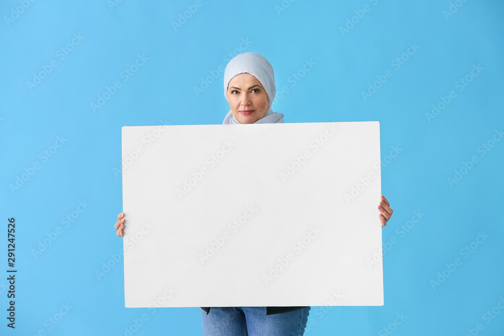 Beautiful mature Muslim woman with blank poster on color background Beautiful mature Muslim woman with blank poster on color background