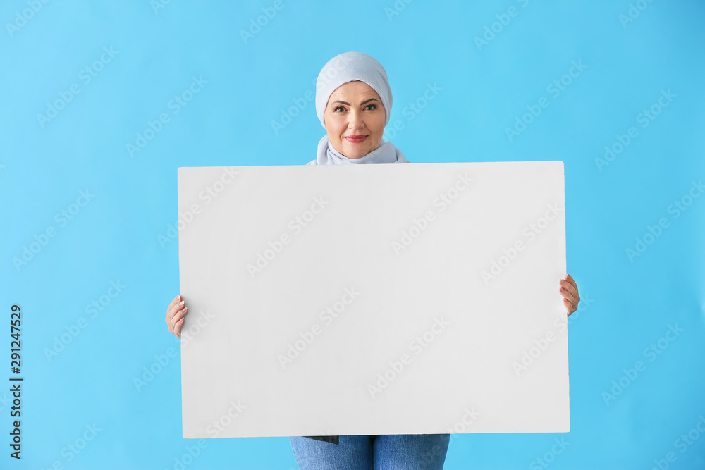 Beautiful mature Muslim woman with blank poster on color background Beautiful mature Muslim woman with blank poster on color background