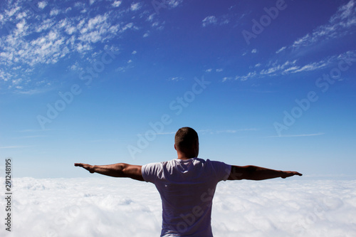 young man with open arms raised above the clouds © Iryna