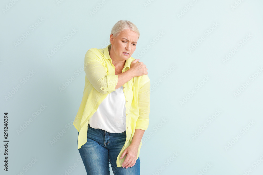 Mature woman suffering from pain in shoulder on light background Mature woman suffering from pain in shoulder on light background