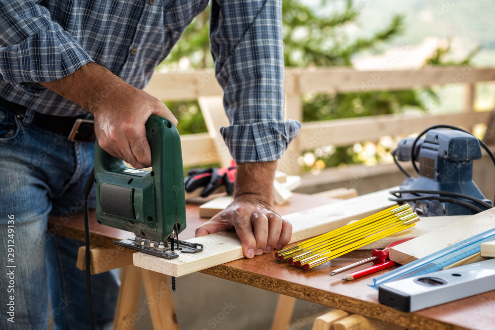 Adult craftsman carpenter with electric saw working on cutting a wooden table. Housework do it yourself. Stock photography.