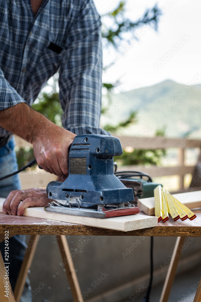 Adult carpenter craftsman with electric sander smoothes a wooden table. Housework do it yourself. Stock photography.