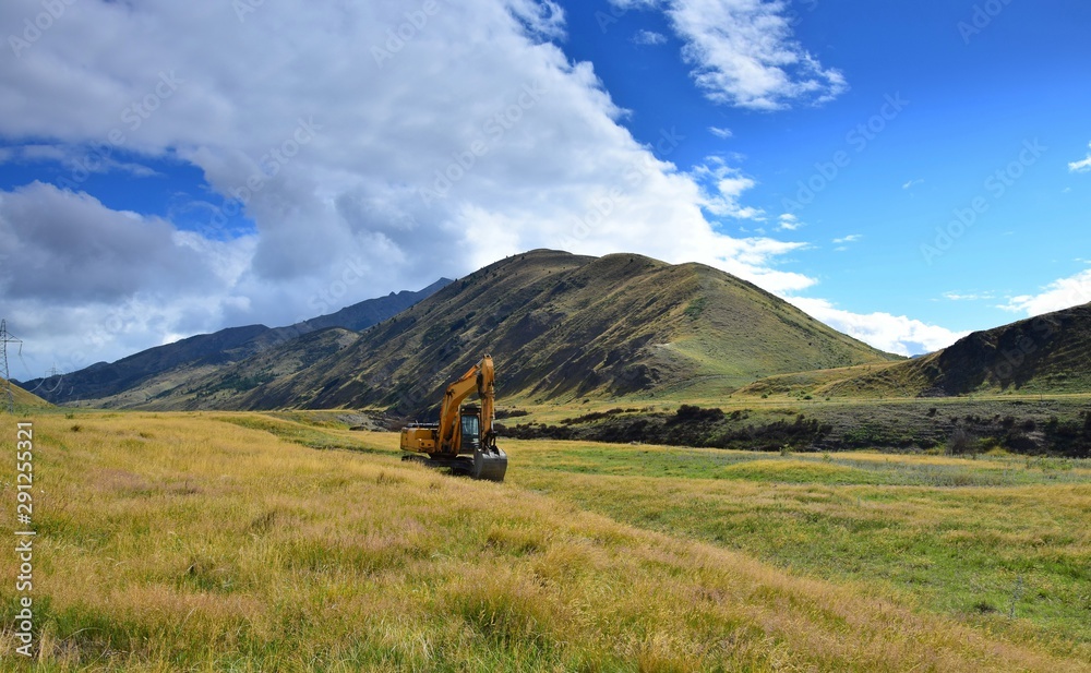 Landscape in New Zealand with a big digger in front of the mountains.