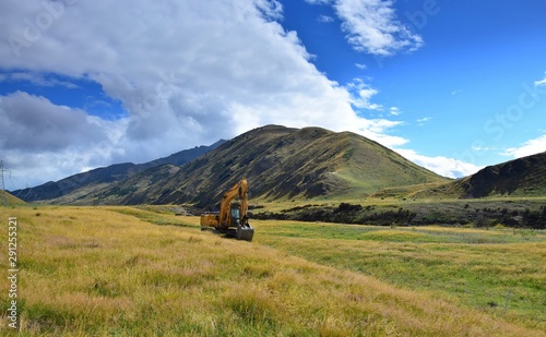 Landscape in New Zealand with a big digger in front of the mountains.