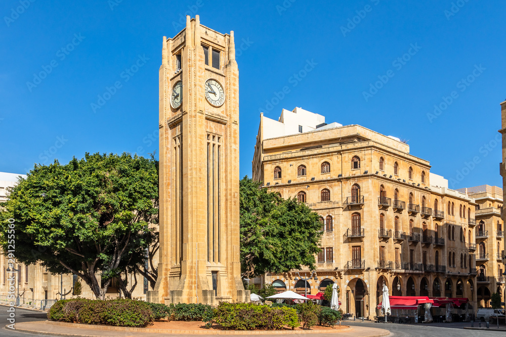 Fototapeta premium Wieża zegarowa na placu Al-Abed Nejmeh z drzewami i budynkami dookoła, Bejrut, Liban