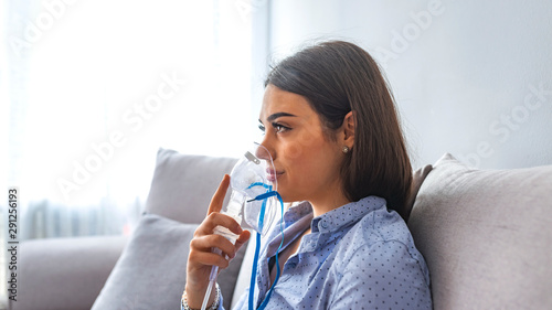 Use nebulizer and inhaler for the treatment. Young woman inhaling through inhaler mask lying on the couch