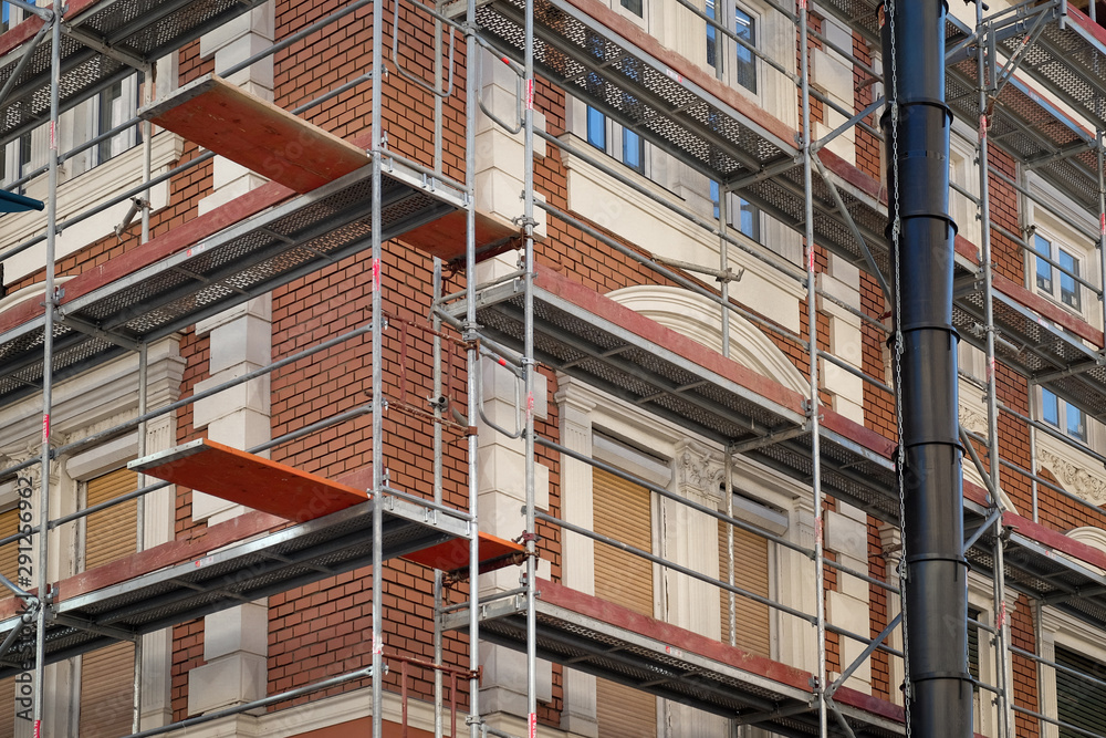 Fototapeta premium Metal scaffolding around red brick old building