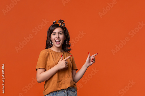 Pretty brunette woman in a t-shirt and beautiful headband pointing with her fingers at the rights side isolated over orange background. Place for ad.