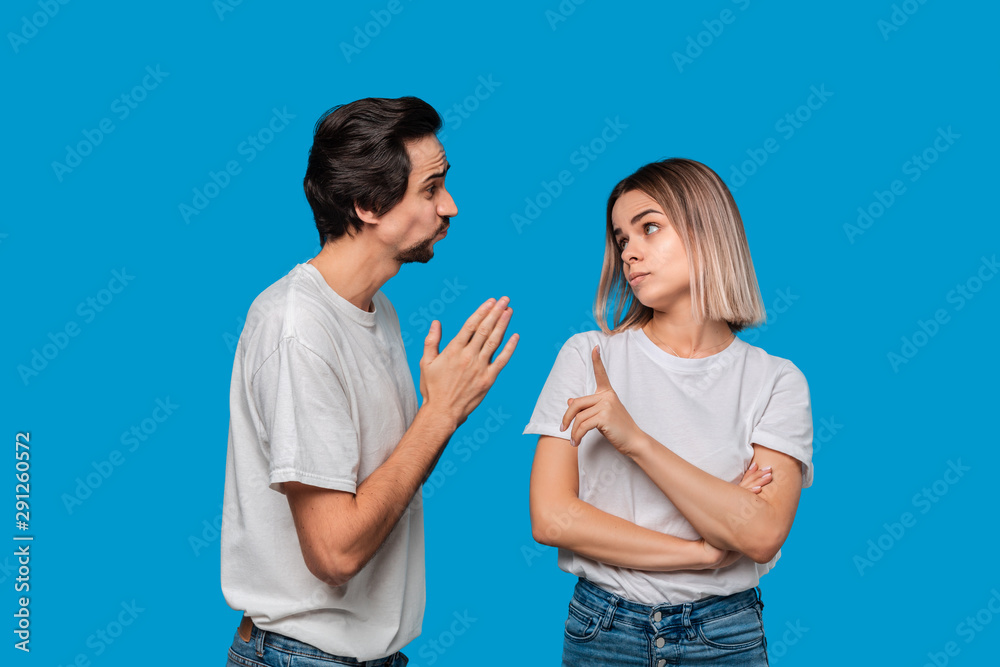 Brunet bearded man with mustaches in white t-shirt and blue jeans asking his girlfriend for forgiveness isolated over blue background. Concept of guilt. Brunet bearded man with mustaches in white t-shirt and blue jeans asking his girlfriend for forgiveness isolated over blue background. Concept of guilt.