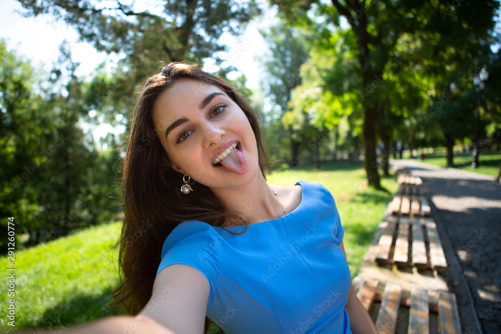 Smiling young woman in a blue dress sits in a park and making selfie with the smartphone. Smiling young woman in a blue dress sits in a park and making selfie with the smartphone.