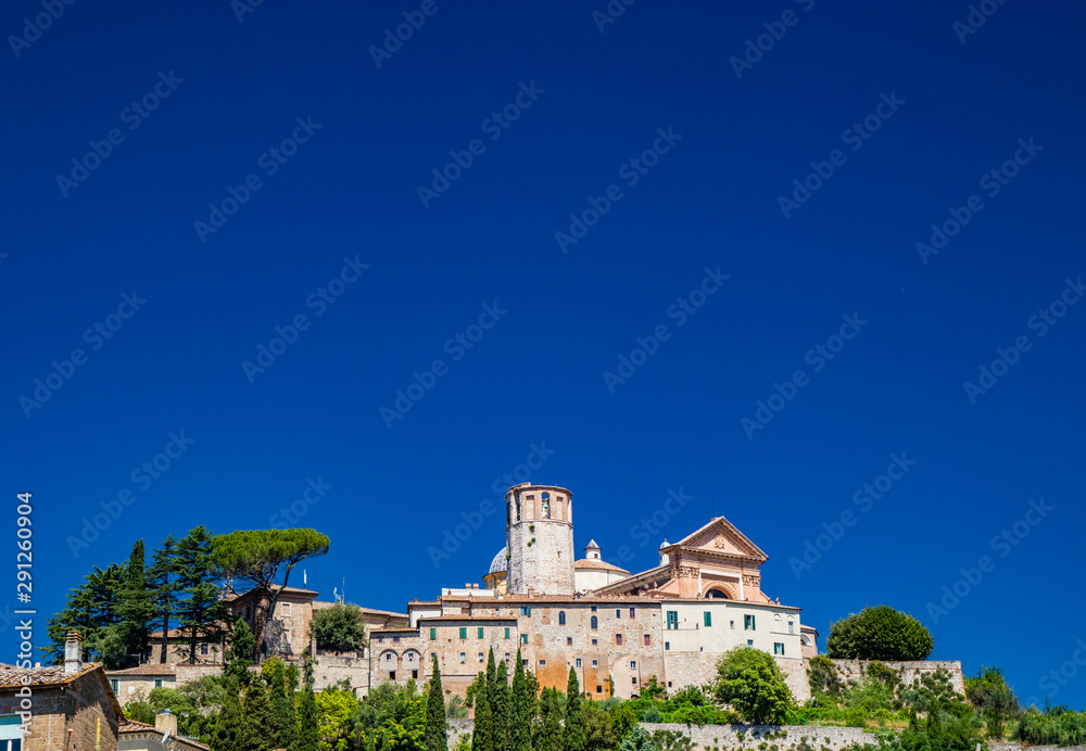 View of the ancient city of Amelia, in Umbria. The boundary wall, the houses and the cathedral with the dodecagonal tower on the top of the hill. The dome, the bell tower. Clear blue sky in the summer