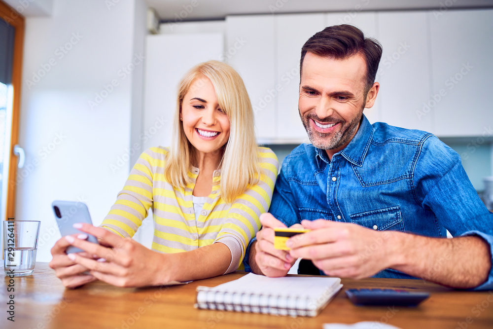 Cheerful couple paying online with smartphone and credit card while managing home budget Cheerful couple paying online with smartphone and credit card while managing home budget