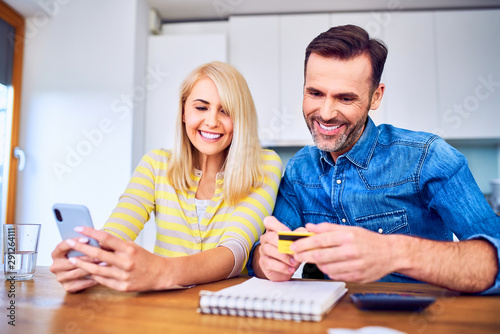 Cheerful couple paying online with smartphone and credit card while managing home budget
