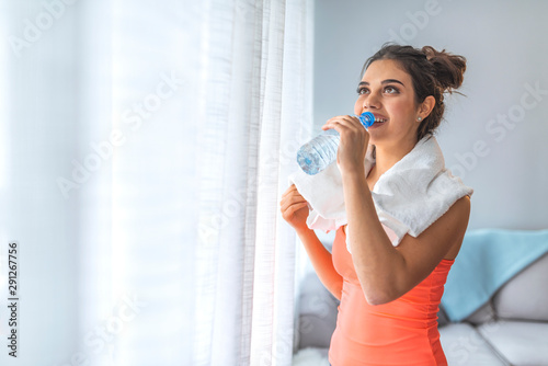 Fit young woman drinking water at the home. Muscular woman taking break after exercise.