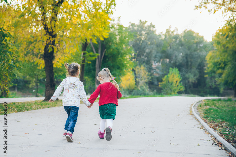 Fototapeta premium two little girls girlfriends playing at autumn city park holding hands