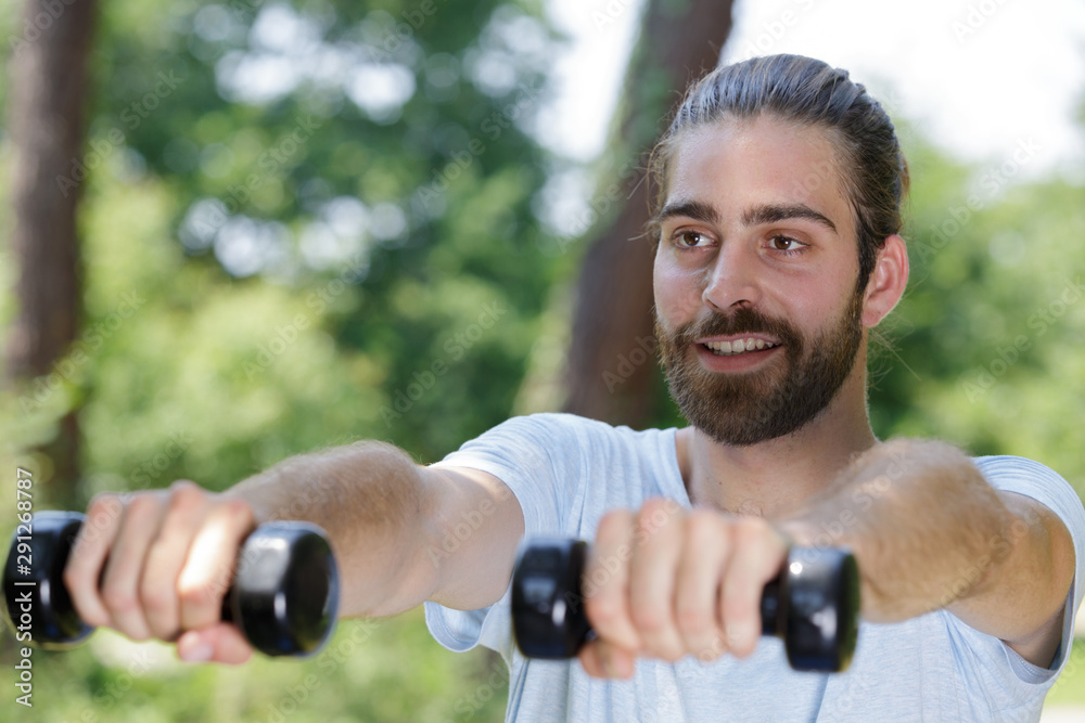 sporty young man training with dumbbells in park