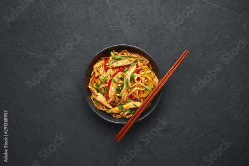 Chicken Schezwan Noodles or Hakka or Chow Mein in black bowl at dark background. Schezwan Noodles is indo-chinese cuisine hot dish with udon noodles, vegetables and chilli sauce. Copy space