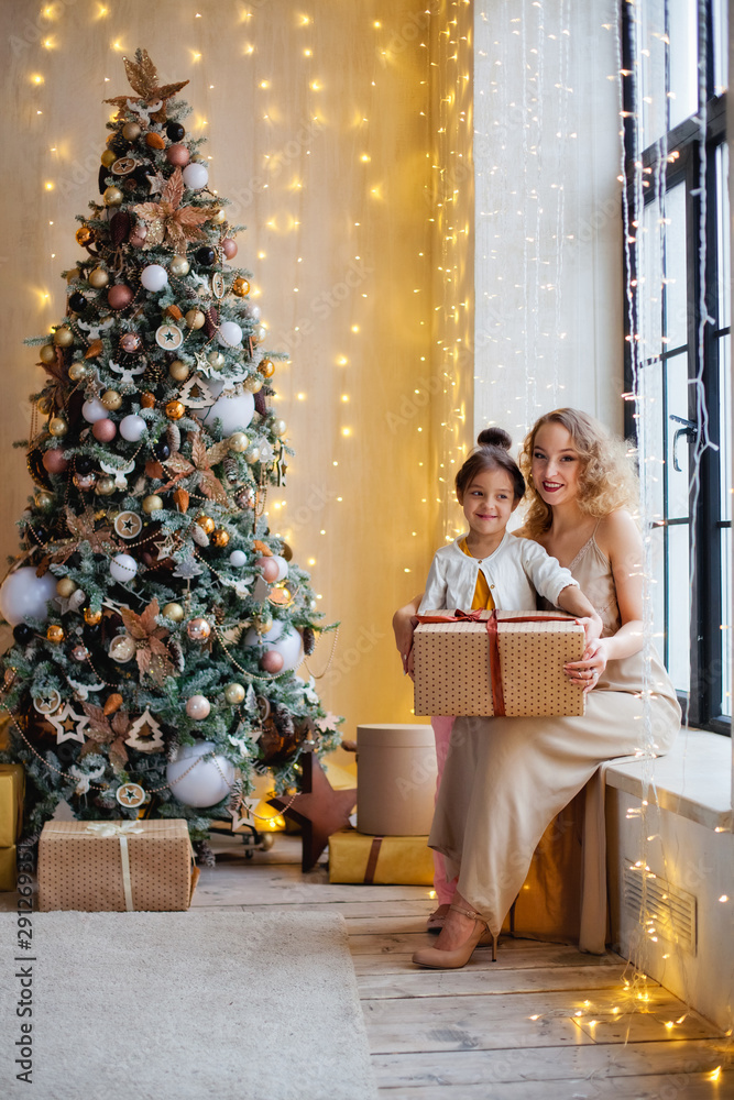 mother and daughter near the Christmas tree sitting with a gift on the windowsill