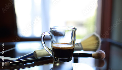 Cup of coffee with the phone and make-up set and brushes on the glass table